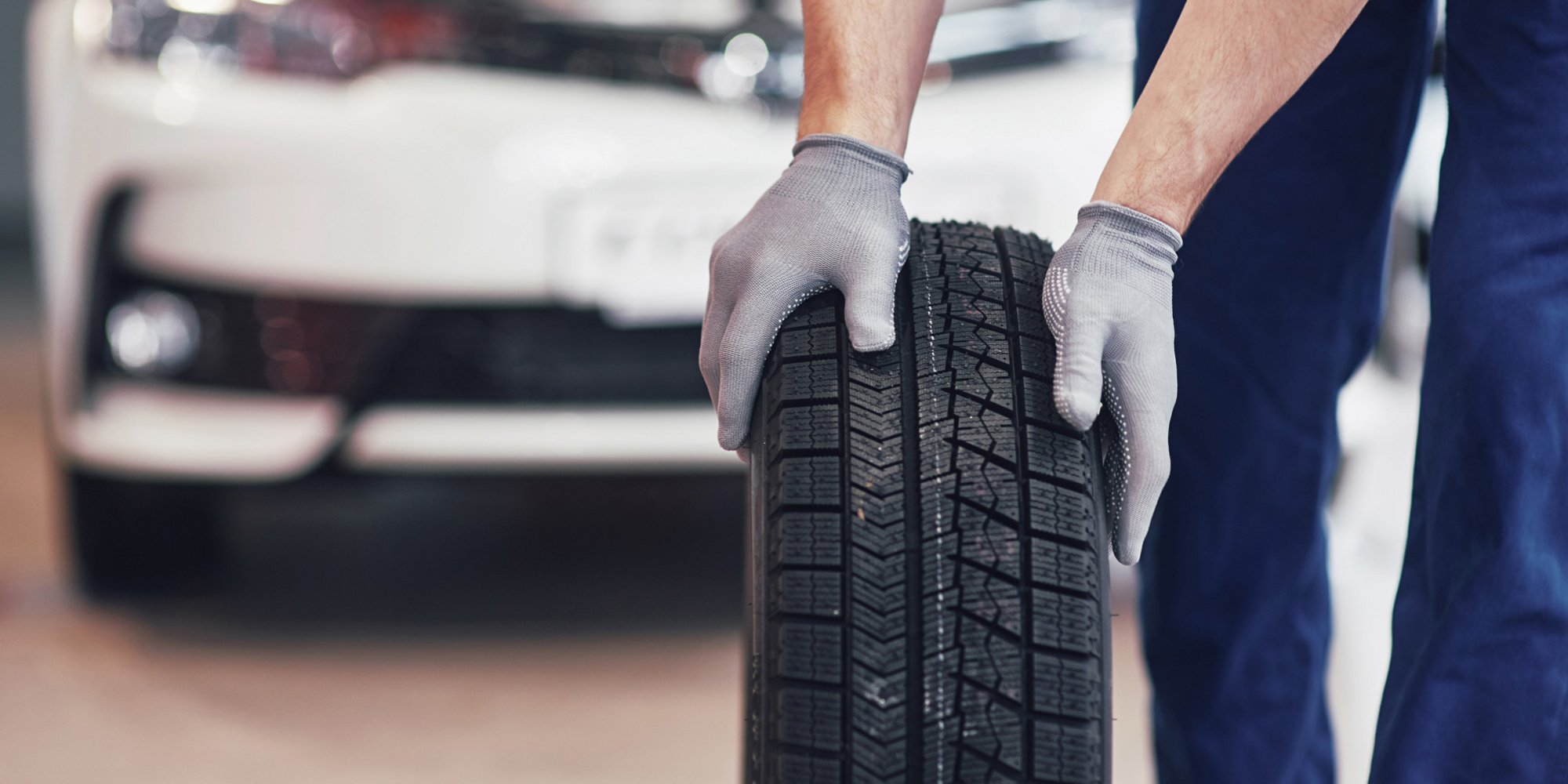 Mitarbeiter rollt einen Reifen vor einem Auto in einer Werkstatt.