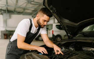 Mechaniker inspiziert konzentriert den Motorraum eines Autos in einer Werkstatt.